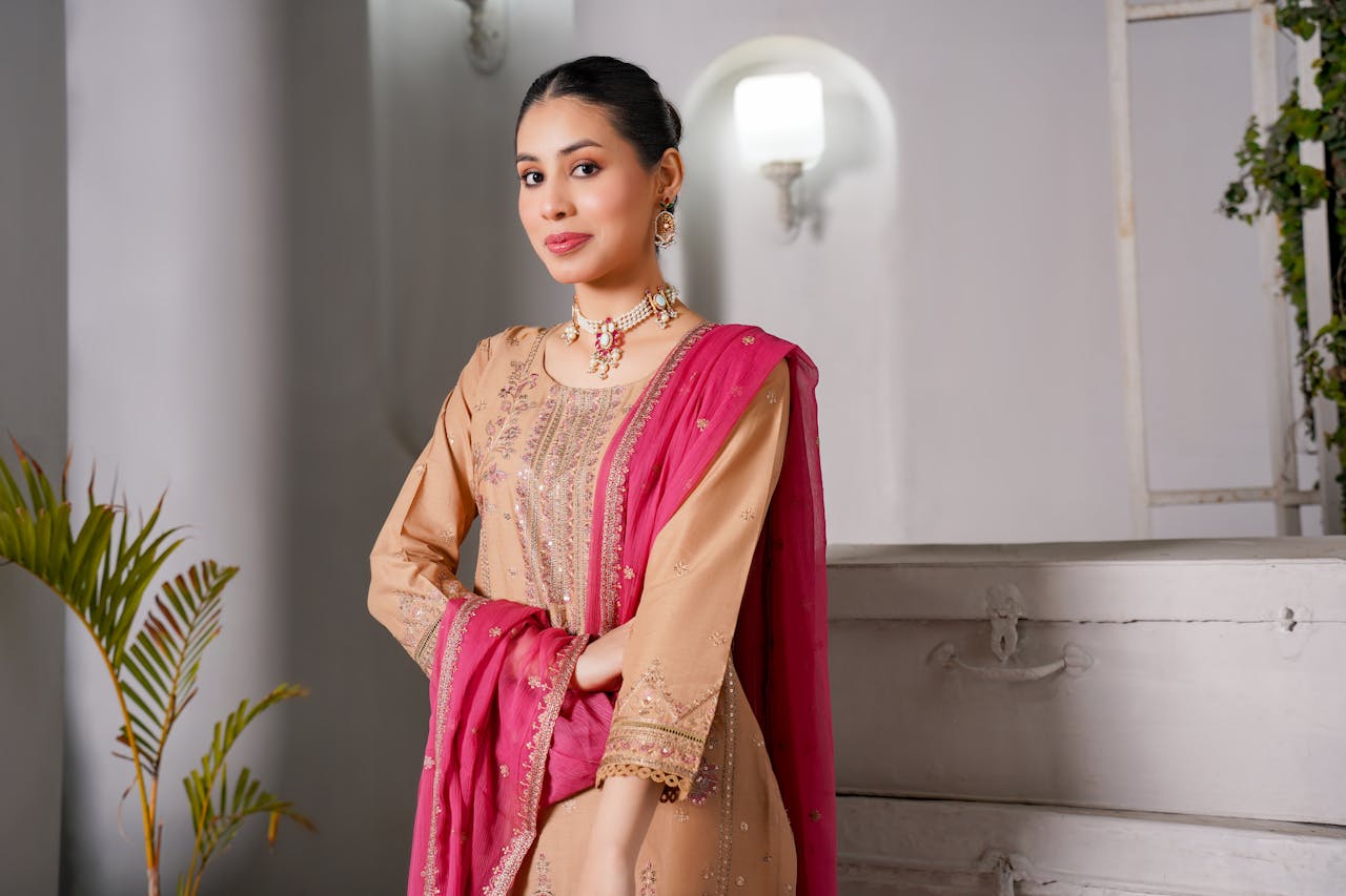 Portrait of a South Asian woman in traditional attire, standing indoors with elegant poise.